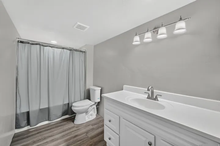 Bathroom featuring a white vanity with integrated sink, brushed nickel faucet, four-light vanity fixture, and wood-finish flooring