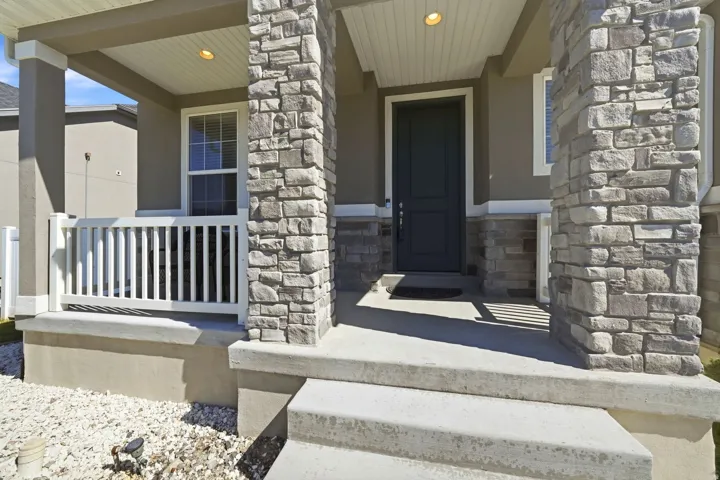 Stone-clad columns, covered porch with beadboard ceiling, paneled entry door, white railing, and decorative rock landscaping