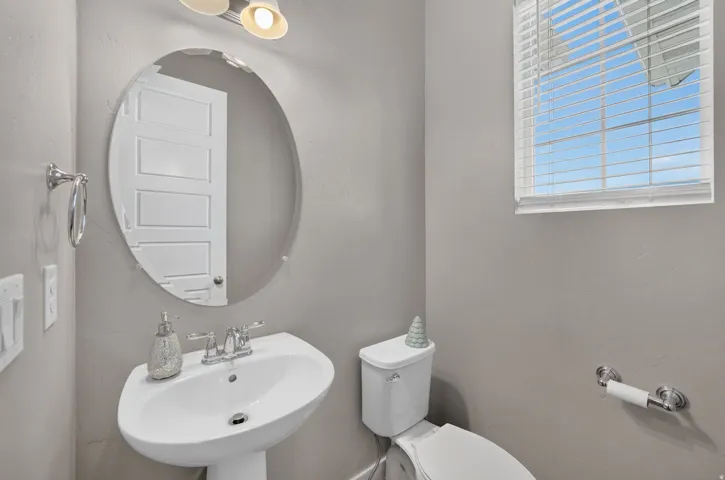 Pedestal sink with chrome fixtures, oval wall mirror, and window with blinds