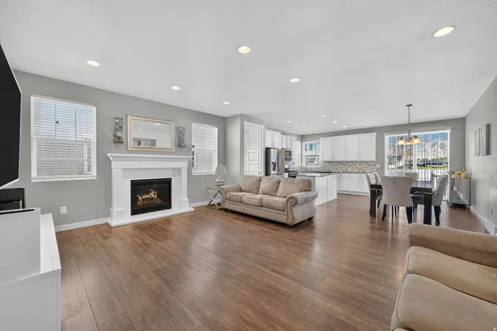 Open concept living area featuring wood-finish flooring, a fireplace with a white mantel, recessed lighting, and a kitchen with white cabinetry and stainless steel appliances