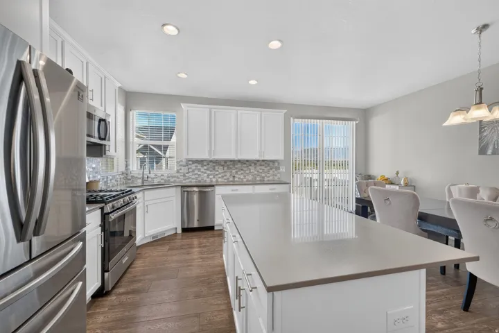 Contemporary kitchen featuring white cabinetry, stainless steel appliances, wood-finish flooring, a center island with a light-toned countertop, and a mosaic tile backsplash