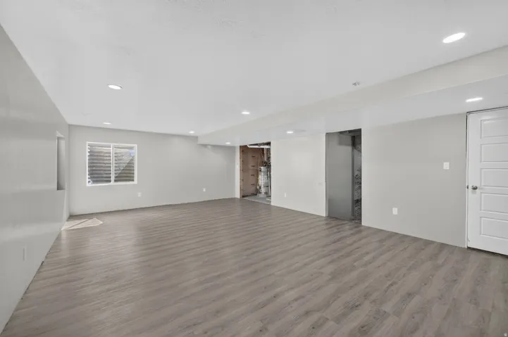 Spacious room featuring light gray walls, recessed lighting, wood-finish flooring, and a white egress window