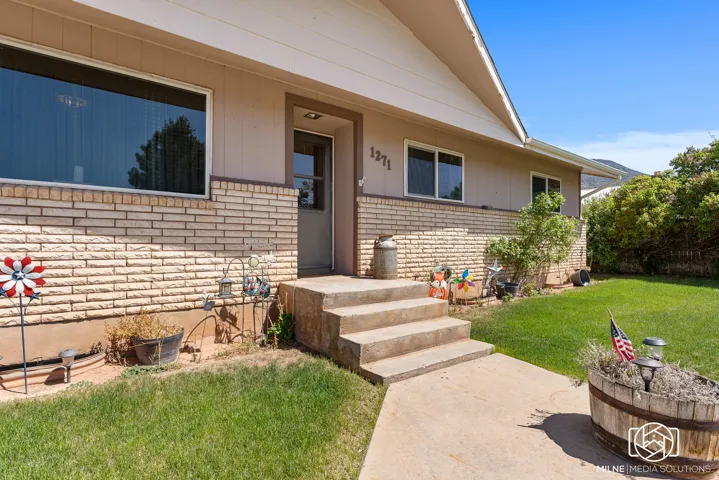 Front exterior featuring brick and siding facade, multiple windows, a concrete walkway, and a landscaped front yard with established plantings
