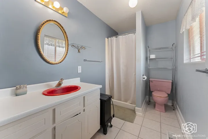 Bathroom featuring a white vanity with an undermount red sink, tiled flooring, a shower with a shower curtain, and a window with blinds