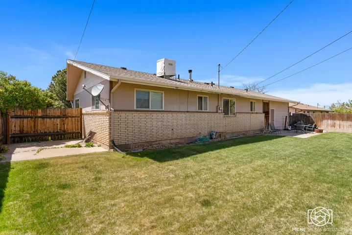Expansive grass lawn with a wood plank fence, concrete patio area, and brick exterior