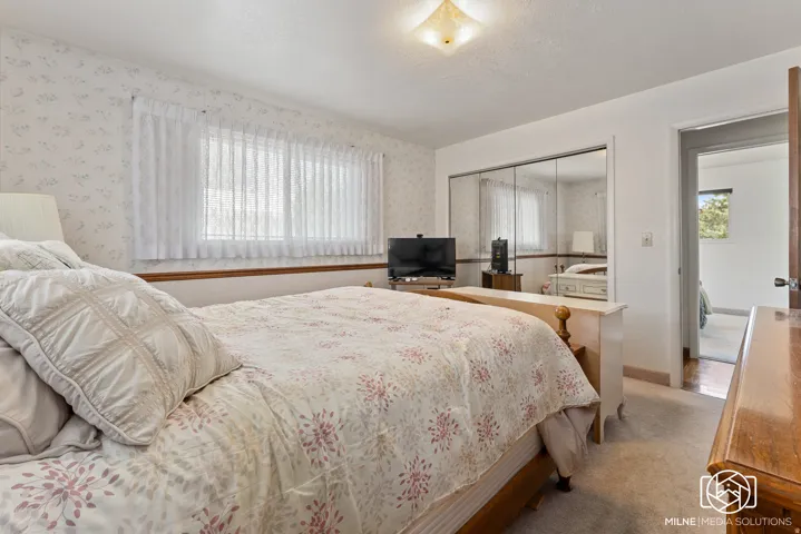 Patterned wallpaper accent, mirrored closet doors, dual windows, and ceiling-mounted light fixture