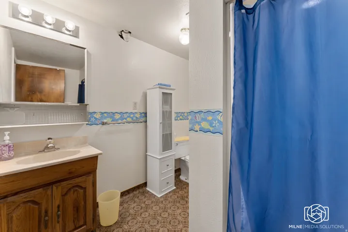 Vanity with a single basin sink, wall-mounted mirror, and overhead lighting