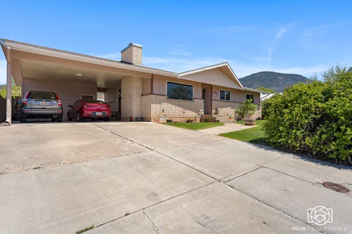 Exterior featuring a covered carport, brick facade, a concrete driveway, and established landscaping