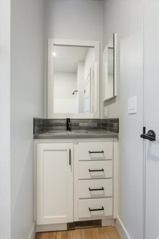 Vanity with white shaker-style cabinetry, matte black hardware, dual undermount sinks, a gray countertop, and a dark tile backsplash