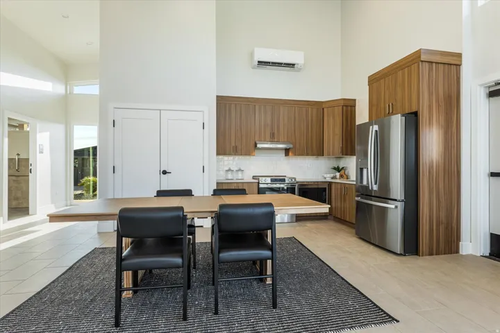 Vaulted ceilings, wood-finish cabinetry, stainless steel appliances, white tile backsplash, and light-toned flooring