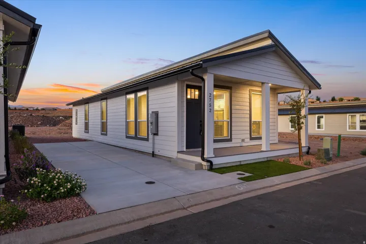 White horizontal siding exterior with dark trim windows, covered front porch, concrete driveway, and low-maintenance landscaping