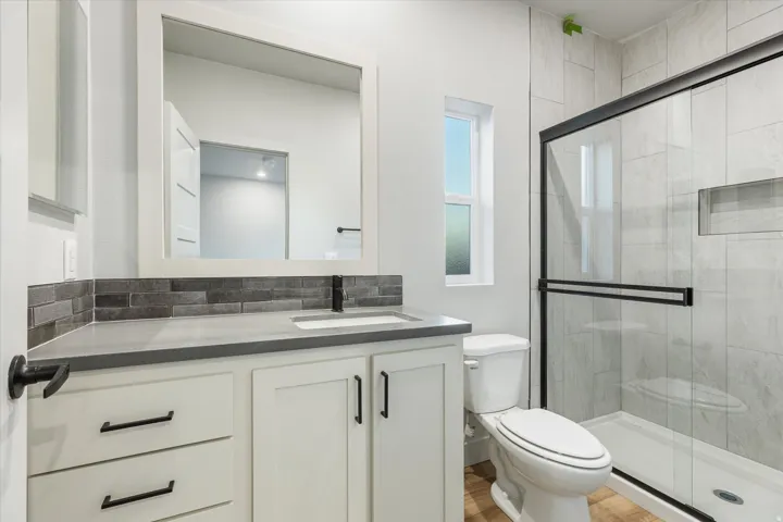 White vanity with matte black hardware, grey countertop, and stone tile backsplash