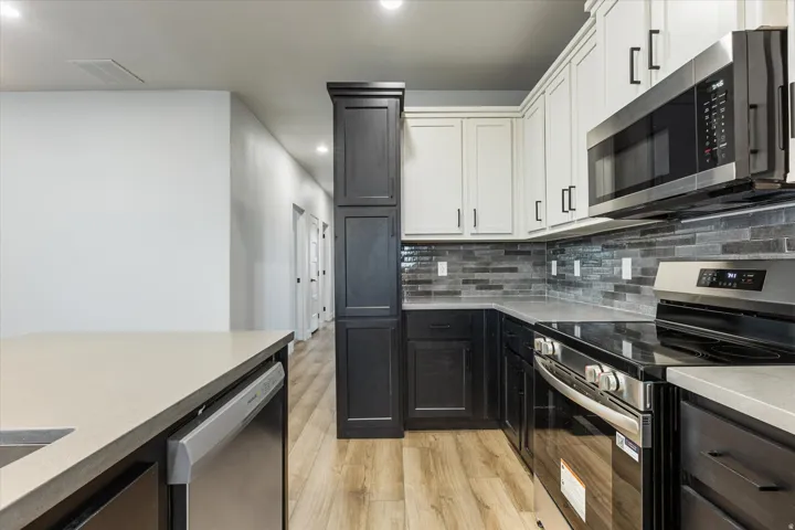 Two-tone cabinetry with black matte hardware, stainless steel appliances, light-toned countertops, and wood-finish flooring