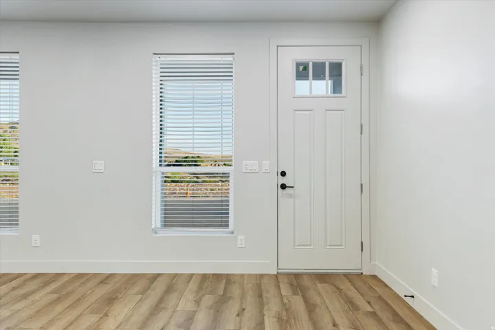 White paneled door with glass inserts, matte black hardware, wood-finish flooring, and white window blinds
