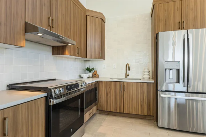 Full kitchen featuring wood-finish cabinetry, stainless steel appliances, white subway tile backsplash, and light-toned countertops