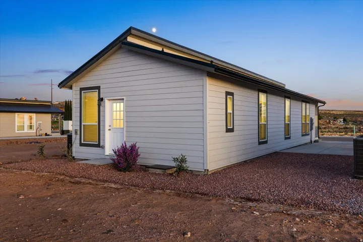 Gray horizontal siding with black-framed windows, a white entry door, and a dark pitched roof