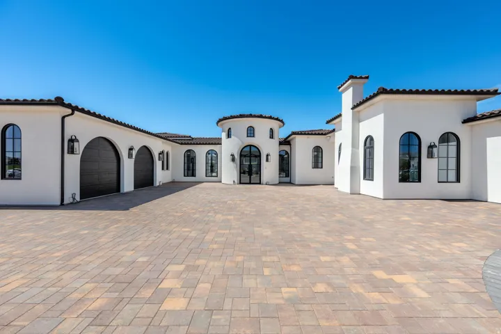 Stucco exterior featuring arched windows, dark tile roof, paved driveway, and custom garage doors