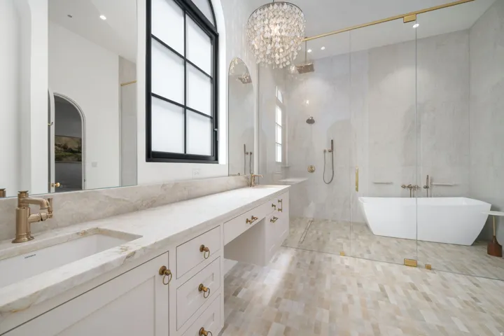 Dual sink vanity with stone countertop, freestanding soaking tub, frameless glass shower enclosure, and intricate floor tiling