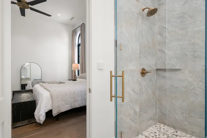 Walk-in shower with large-format tile walls, pebble-style flooring, and brass fixtures