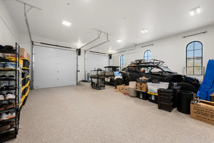 Spacious garage featuring two overhead doors, epoxy flooring, multiple recessed light fixtures, and arched windows
