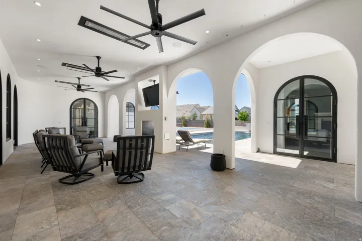 Covered patio featuring arched doorways, stone-finish flooring, multiple ceiling fans, recessed lighting, and a mounted television