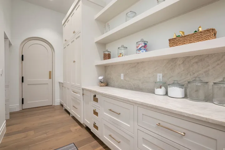 Arched entryway with a paneled door, extensive built-in cabinetry, wood-finish flooring, stone-finish countertops, and open shelving