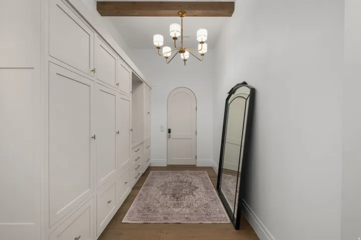 Built-in cabinetry with paneling, wood-finish flooring, exposed ceiling beam, arched doorway, and a brass chandelier