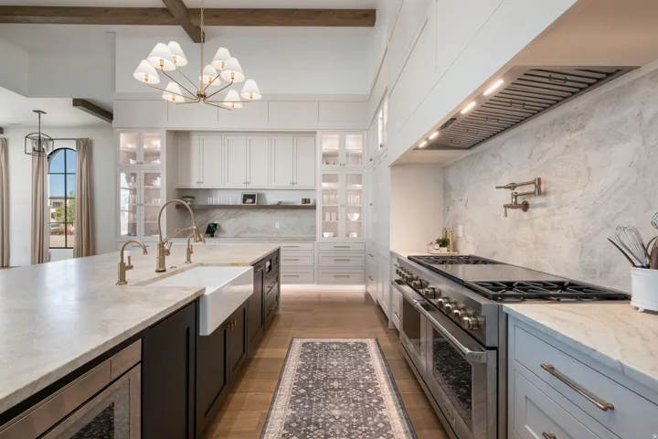 Gourmet kitchen featuring a large island with a farmhouse sink, stone countertops, a professional-grade range with a pot filler, and extensive built-in cabinetry with glass-front accents