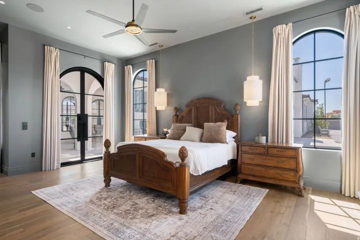 Hardwood-style flooring, a ceiling fan with integrated lighting, a double arched doorway, and two arched windows with grid patterns
