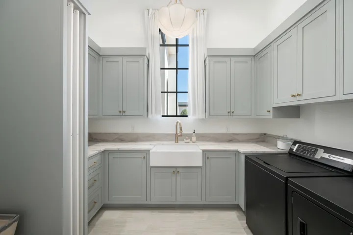 U-shaped cabinetry with panel doors, stone countertops, a large farmhouse sink with a gooseneck faucet, and a large window with high ceilings