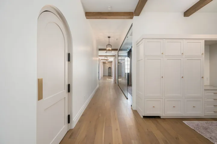 Arched doorway, wood-finish flooring, exposed ceiling beams, built-in cabinetry, and modern pendant lighting