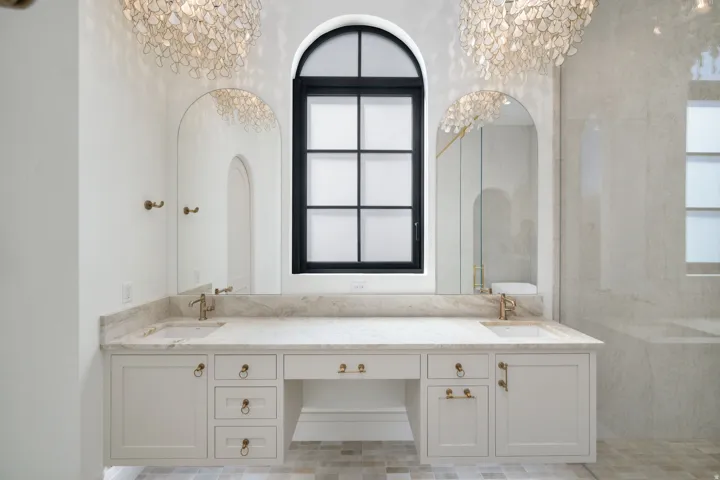 Double vanity featuring an arched window, decorative light fixtures, and dual sinks