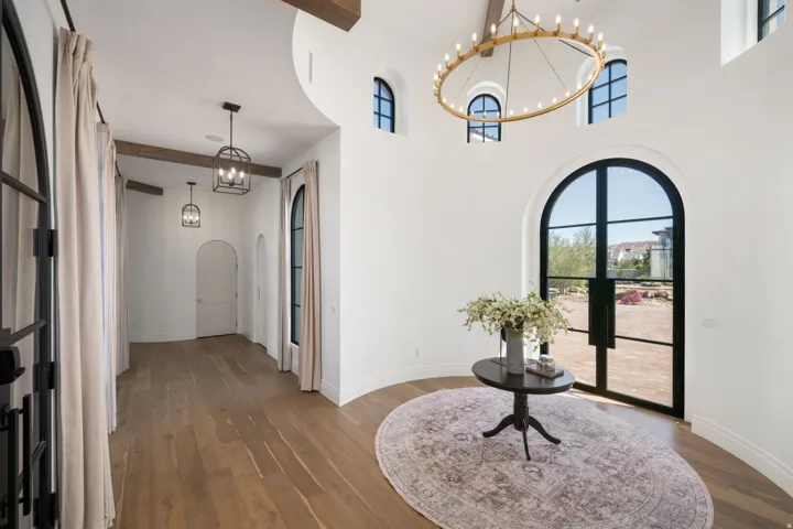 Arched iron-frame entry doors, high ceilings with exposed wood beams, and a large circular chandelier