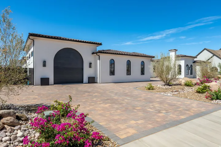 Stucco exterior with arched garage door, barrel tile roofing, paver driveway, and arched windows