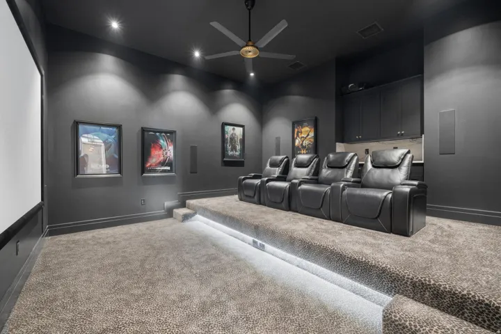 Dedicated media room featuring tiered seating with integrated step lighting, a built-in wet bar with cabinetry, recessed ceiling lighting, and a ceiling fan