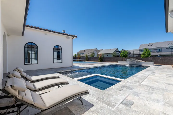 Backyard featuring a rectangular pool with an integrated spa, stone-tile patio, and a stucco exterior with arched windows