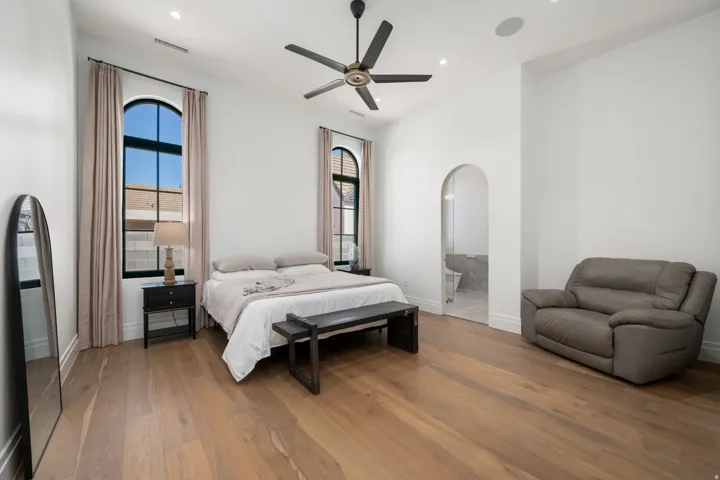 Hardwood flooring, arched windows, ceiling fan, recessed lighting, and an arched doorway leading to a bathroom