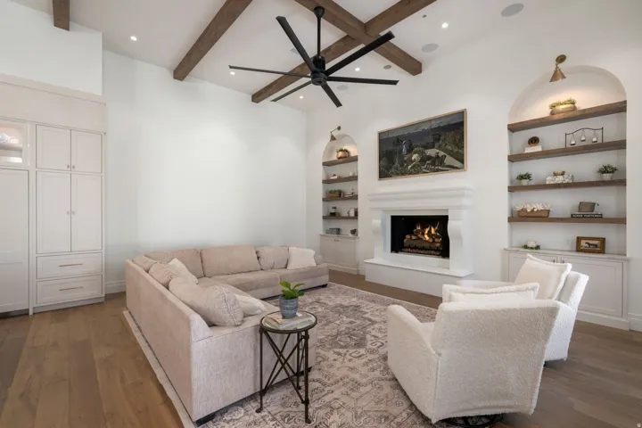 Vaulted ceiling with wood beams, recessed lighting, white stone fireplace, built-in shelving, and wood-finish flooring