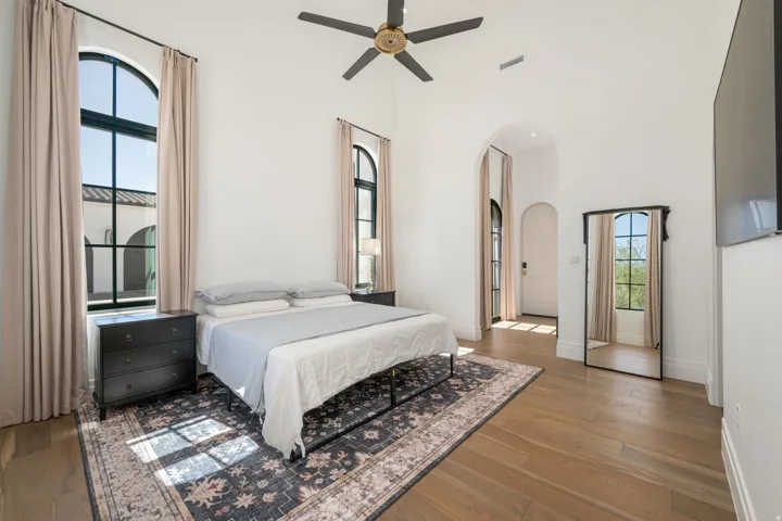 Wood-finish flooring, arched windows with dark framing, vaulted ceilings, and a ceiling fan