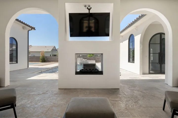 Covered outdoor living area with a built-in fireplace, wall-mounted television, and arched doorways