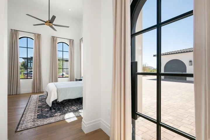 Arched windows with dark frames, high ceilings, wood-finish flooring, and a contemporary ceiling fan
