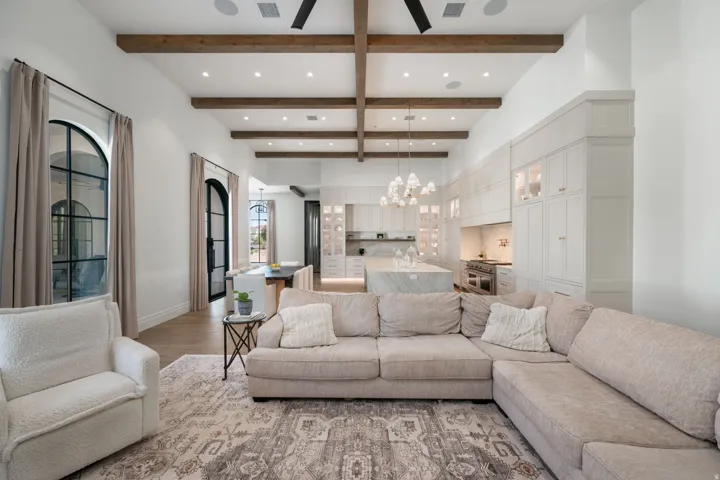 Vaulted ceiling with wood-finish beams, arched windows with dark frames, wood-finish flooring, built-in cabinetry, and integrated kitchen appliances