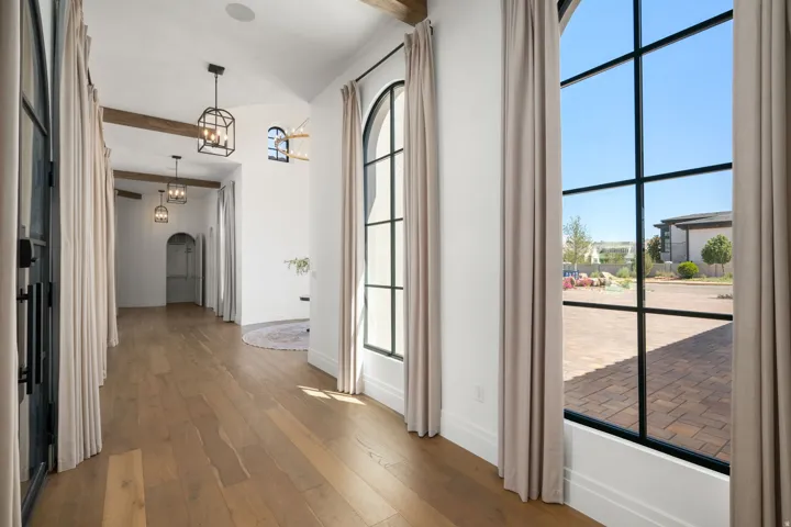 Arched windows with black framing, wood-finish flooring, vaulted ceilings with exposed wood beams, and wrought iron light fixtures