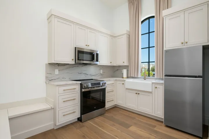 Kitchen featuring stainless steel appliances, wood-finish flooring, white cabinetry, a farmhouse sink, and a built-in bench