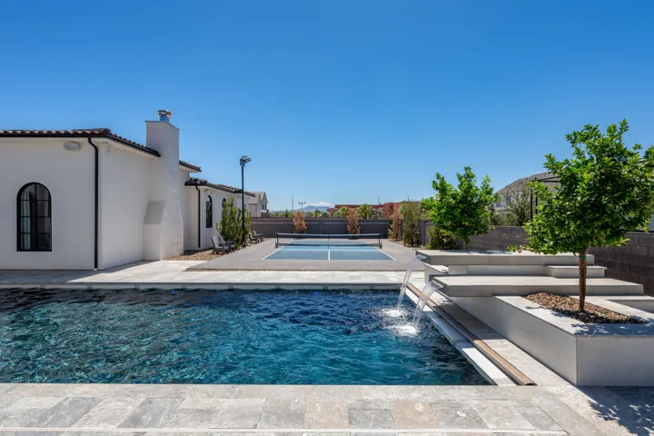 Resort-style backyard featuring a dark bottom swimming pool with water features, a built-in spa, a multi-sport court, and tiered hardscaping