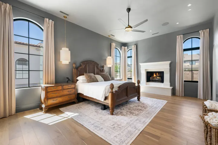 Hardwood flooring, arched windows with dark framing, recessed lighting, ceiling fan, and a fireplace with a white mantel