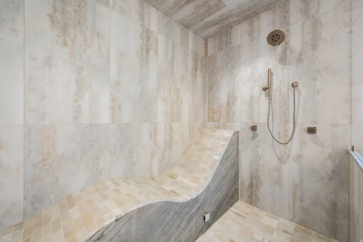 Spacious walk-in shower with large-format wall tiles, a built-in tiled bench, and a rain shower head with a handheld sprayer