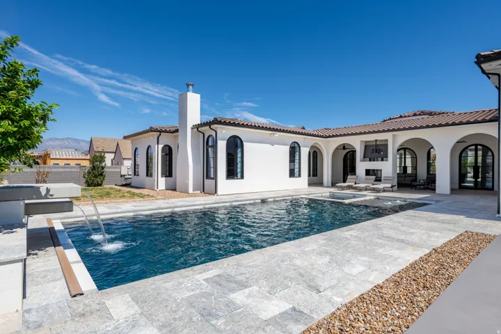 Mediterranean-inspired exterior with a tile roof, an integrated swimming pool with water features, a separate spa, an outdoor fireplace, and an expansive paver patio