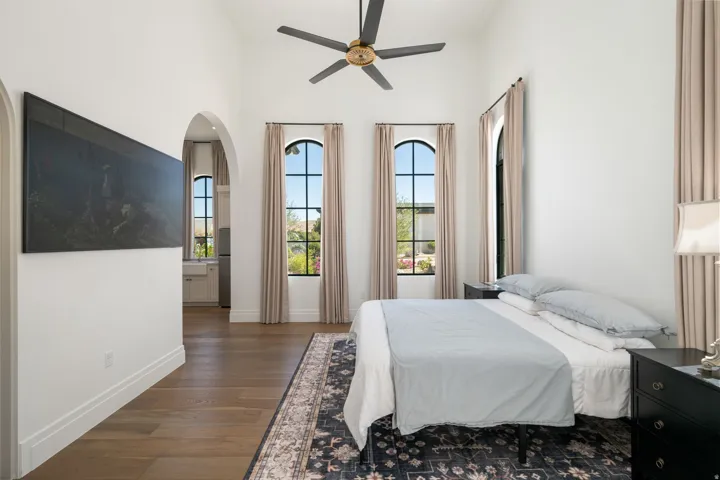 Vaulted ceiling with a ceiling fan, arched windows, and wood-finish flooring