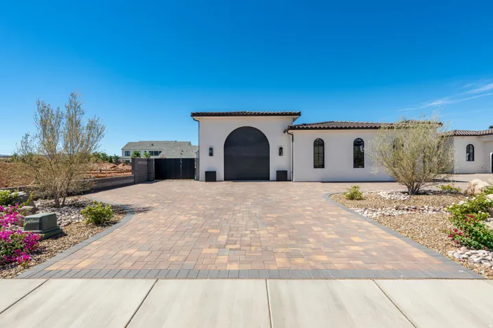 Stucco exterior with a tiled roof, arched garage entry, arched windows, and a paver driveway